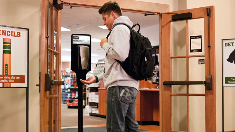 Student using a hand sanitizer dispenser in a school hallway
