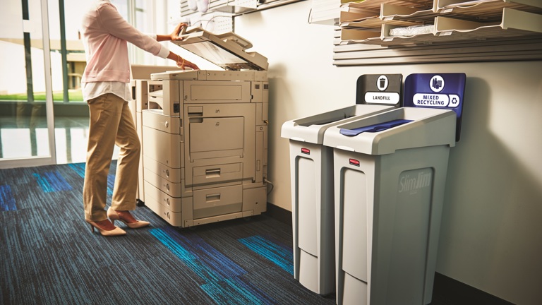 Office worker using copier next to recycling and landfill bins