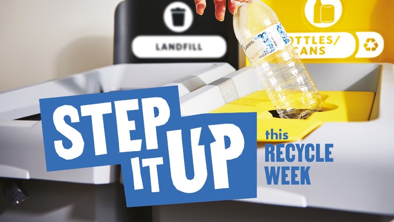 Hand placing plastic bottle in recycling bin next to landfill bin