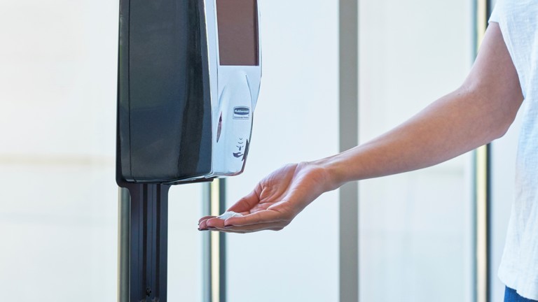 Hand using a touchless sanitizer dispenser in a public area.