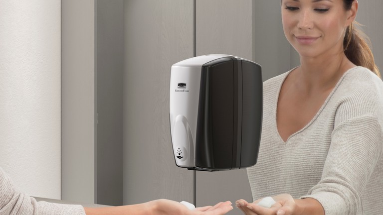 Woman using a wall-mounted automatic soap dispenser in a modern bathroom setting.