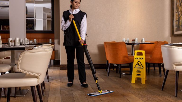 Restaurant worker mopping wooden floor near caution wet floor sign
