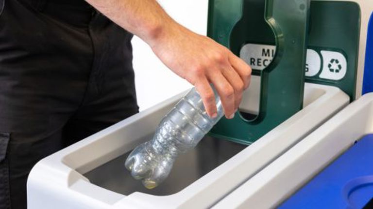 Hand recycling plastic bottle in designated bin.