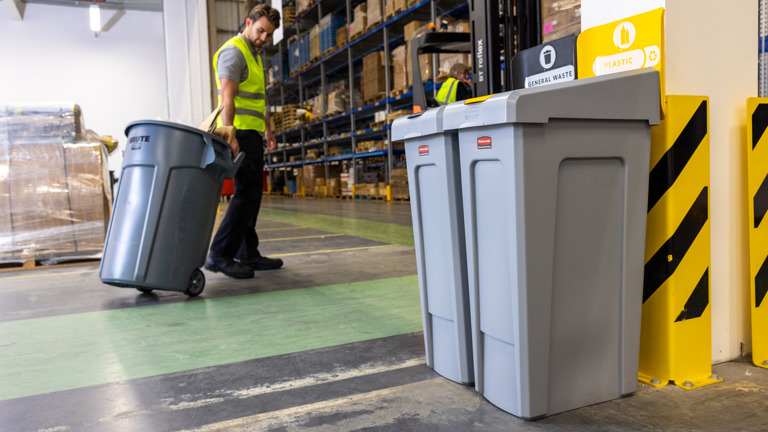Warehouse worker in high visibility vest moving a large trash bin